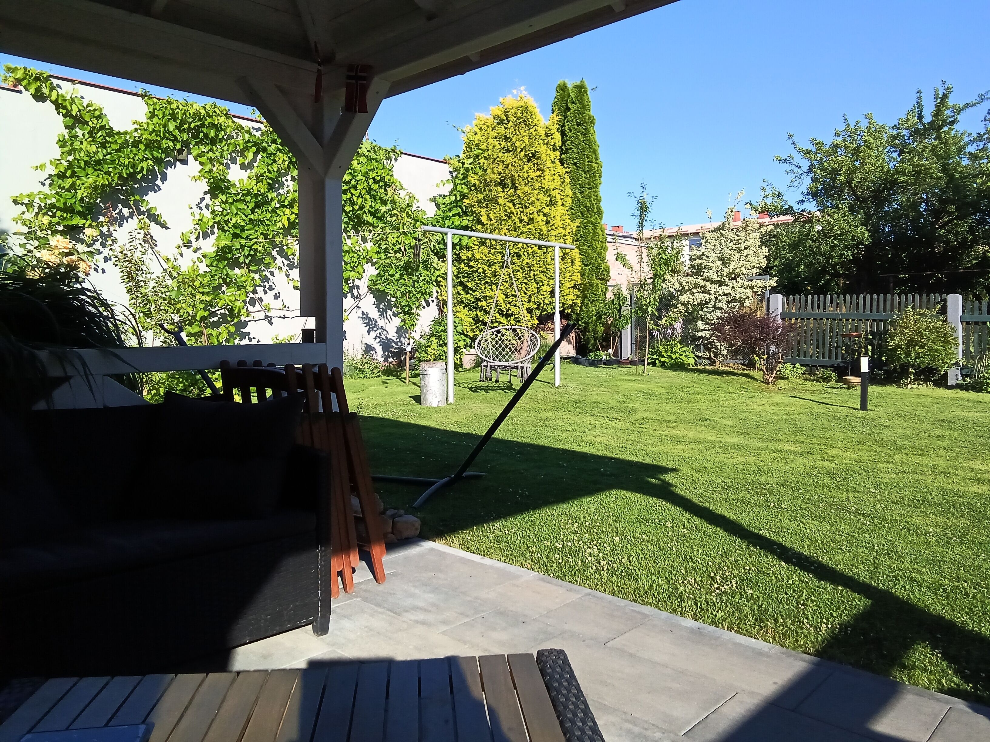 Un patio con zona de estar techada, césped y un parque infantil.