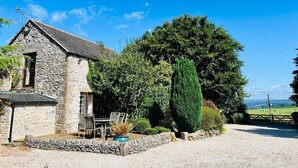 A stone building with a sloped roof, a patio with outdoor furniture, and a well-maintained garden. - Fox Cottage / Luxury 2 Bed (sleeps 4) with stunning views and 4 acre dog field (Matlock)