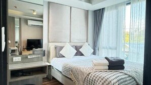 A modern hotel room with a bed, a TV, a desk, and a large window. - 6th Avenue Surin by Win217 (Choeng Thale)