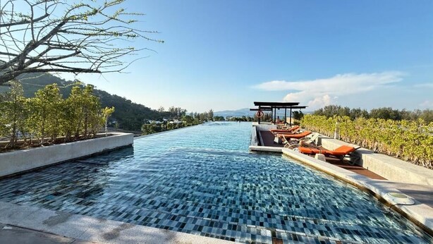 A swimming pool with lounge chairs and a pergola, surrounded by greenery and hills. - 6th Avenue Surin by Win217 (Choeng Thale)