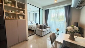 A modern living room with a sofa, a dining table, and a kitchen area with cabinets and a refrigerator. - 6th Avenue Surin by Win217 (Choeng Thale)