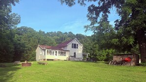 Ein Haus mit Veranda, einer kleinen Terrasse und einem Garten mit Rasen und Picknicktisch.