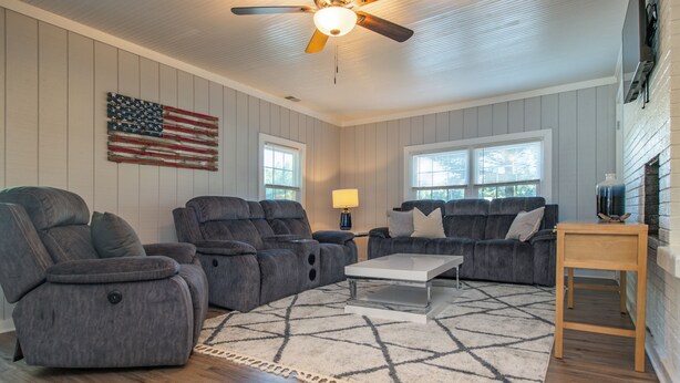 A living room with a ceiling fan, a large American flag, two gray sofas, a coffee table, and a wooden side table.
