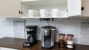 A kitchen with a coffee maker, a water dispenser, and a set of white mugs on a shelf.