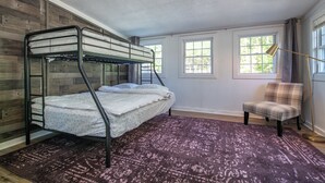 A bunk bed with a patterned rug, a chair, and windows with curtains.