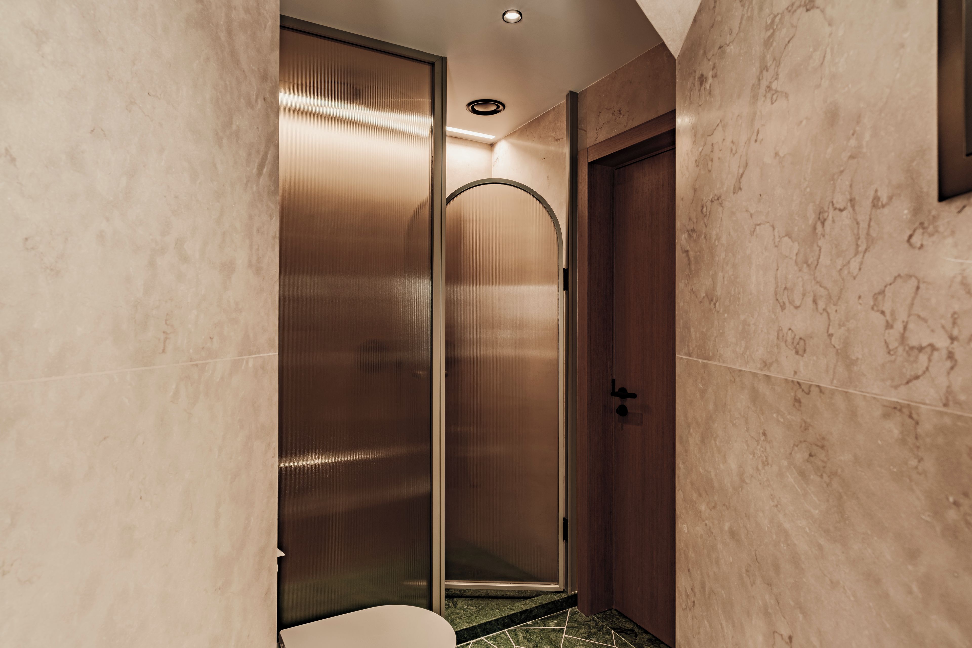 A modern bathroom with a glass-enclosed shower, a wooden door, and marble walls.