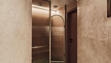 A modern bathroom with a glass-enclosed shower, a wooden door, and marble walls.