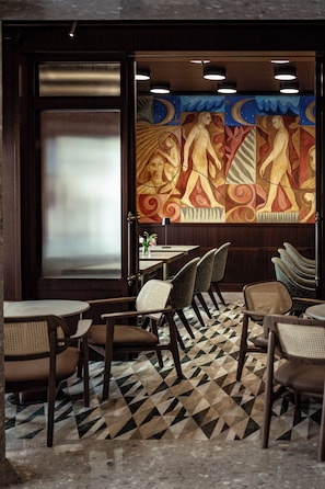 A restaurant interior with a geometric patterned floor, wooden chairs, tables, and a mural with abstract figures. - Romègas Hotel (Valletta)