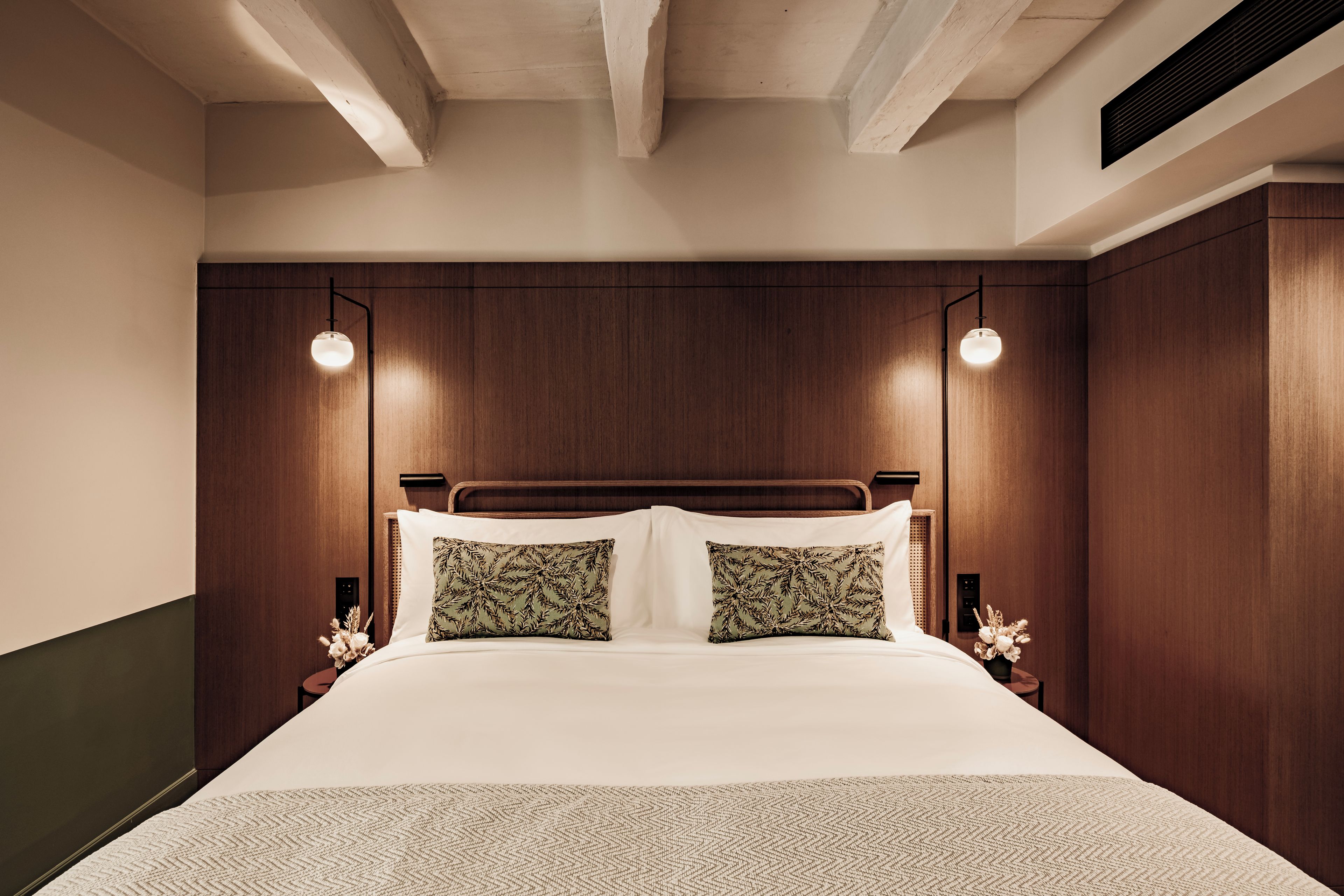 Un dormitorio moderno con cabecera de madera, dos lámparas de noche y una cama con ropa blanca.