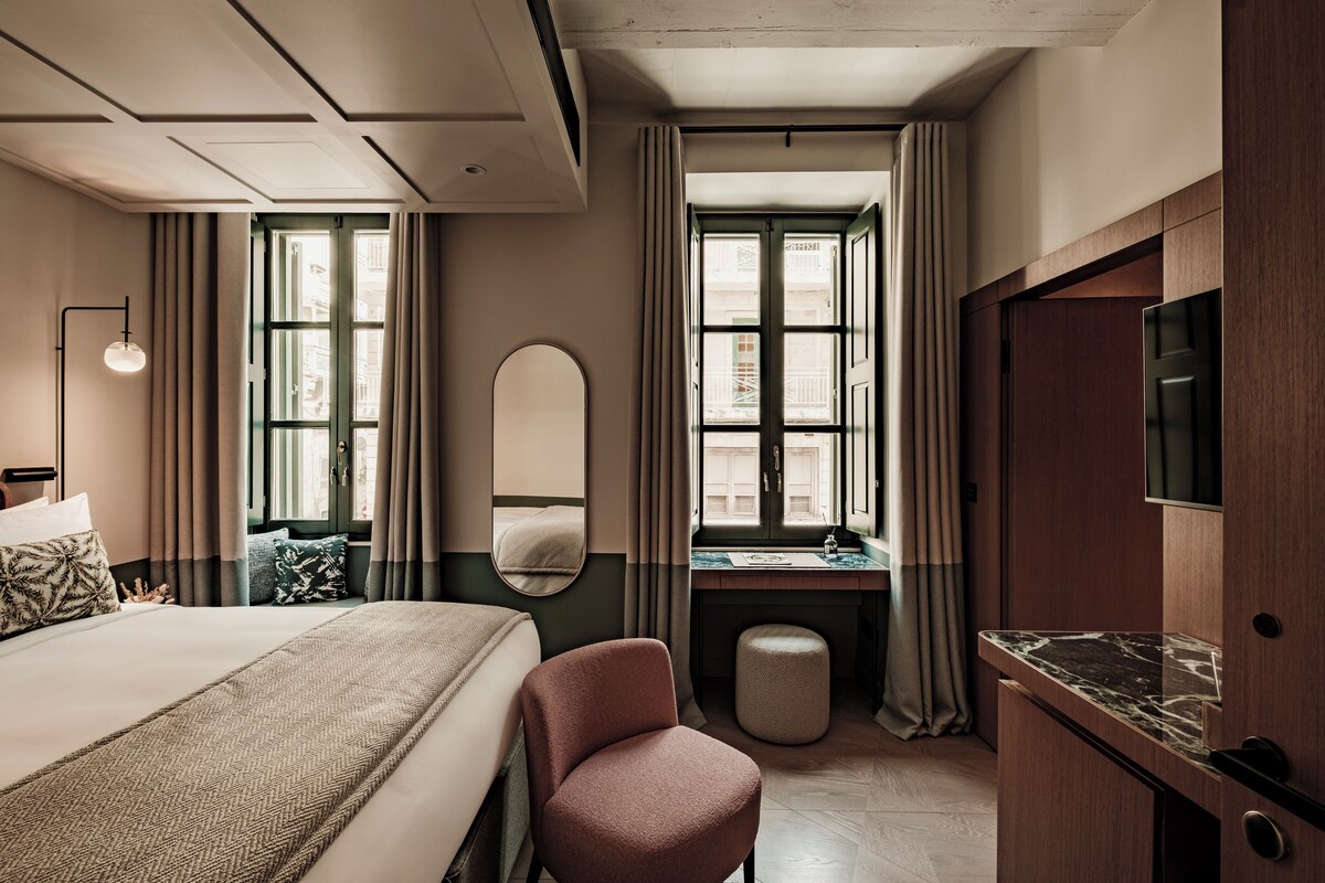 A hotel room with a bed, a desk, a chair, a mirror, and a TV.