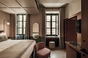 Una habitación de hotel con cama, escritorio, silla, espejo y televisor.