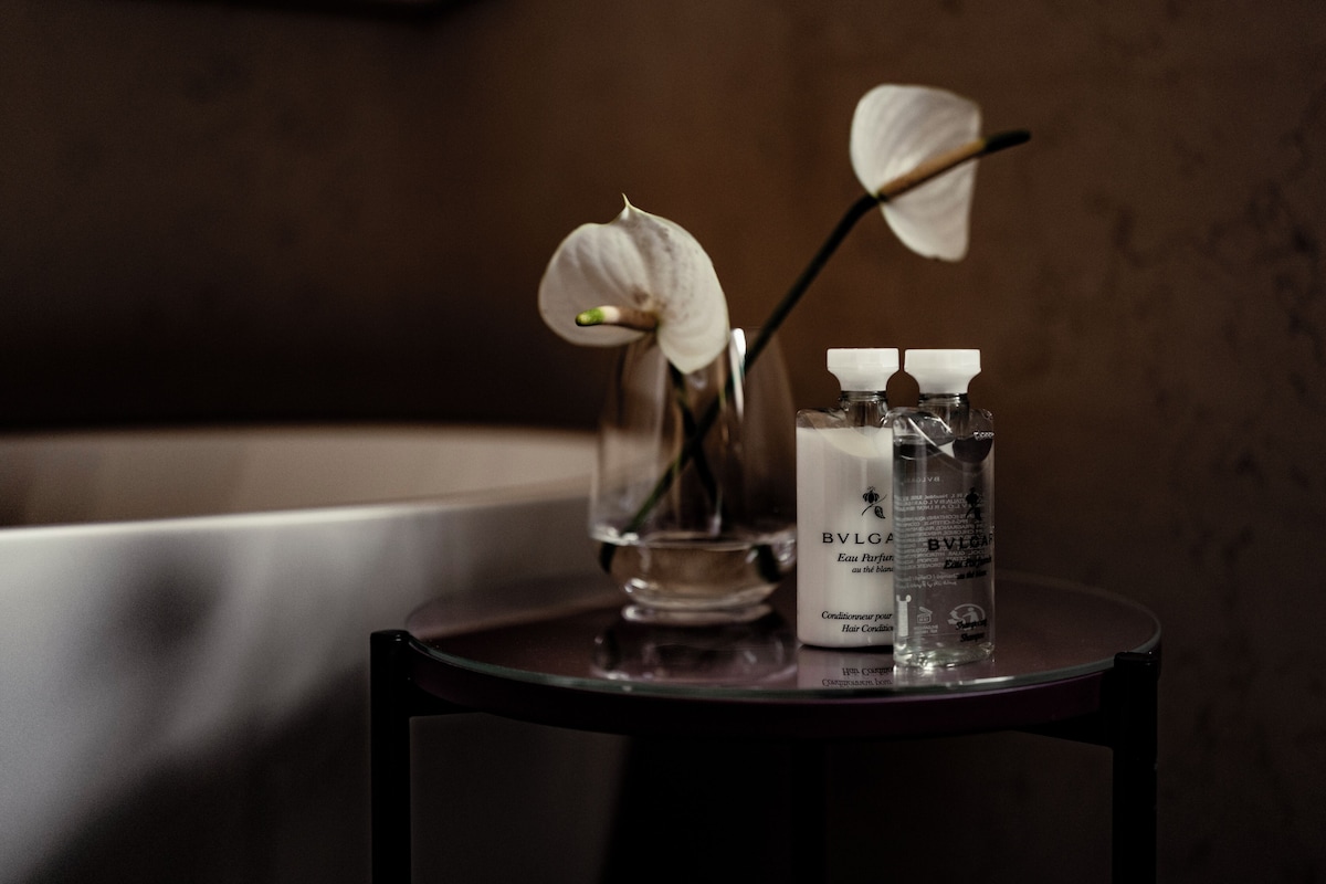 A bathroom with a bathtub, a glass vase with an orchid, and two bottles of BVLGA hair conditioner.