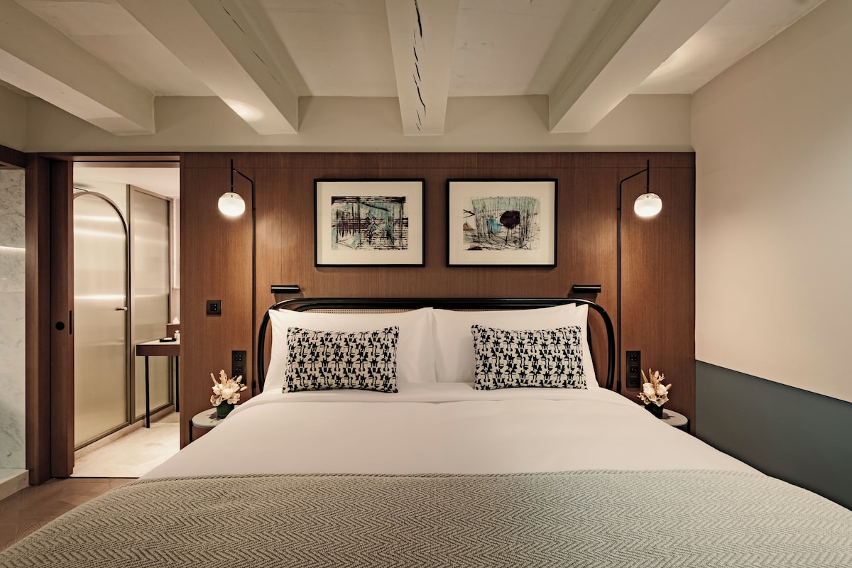 A modern bedroom with a large bed, two wall-mounted lamps, and two framed artworks.
