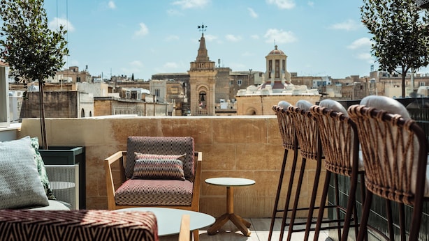 Eine Dachterrasse mit gestreuter Couch, einem kleinen runden Tisch und einem Stuhl mit Webstuhl-Rücken.