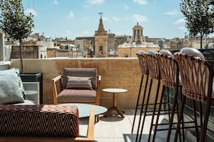 En tagterrasse med en stribet sofa, et lille rundt bord og en stol med en flettet ryg.