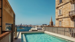 Ein Pool auf dem Dach mit Blick auf die Stadt, einem Holzgeländer und blauem Himmel.