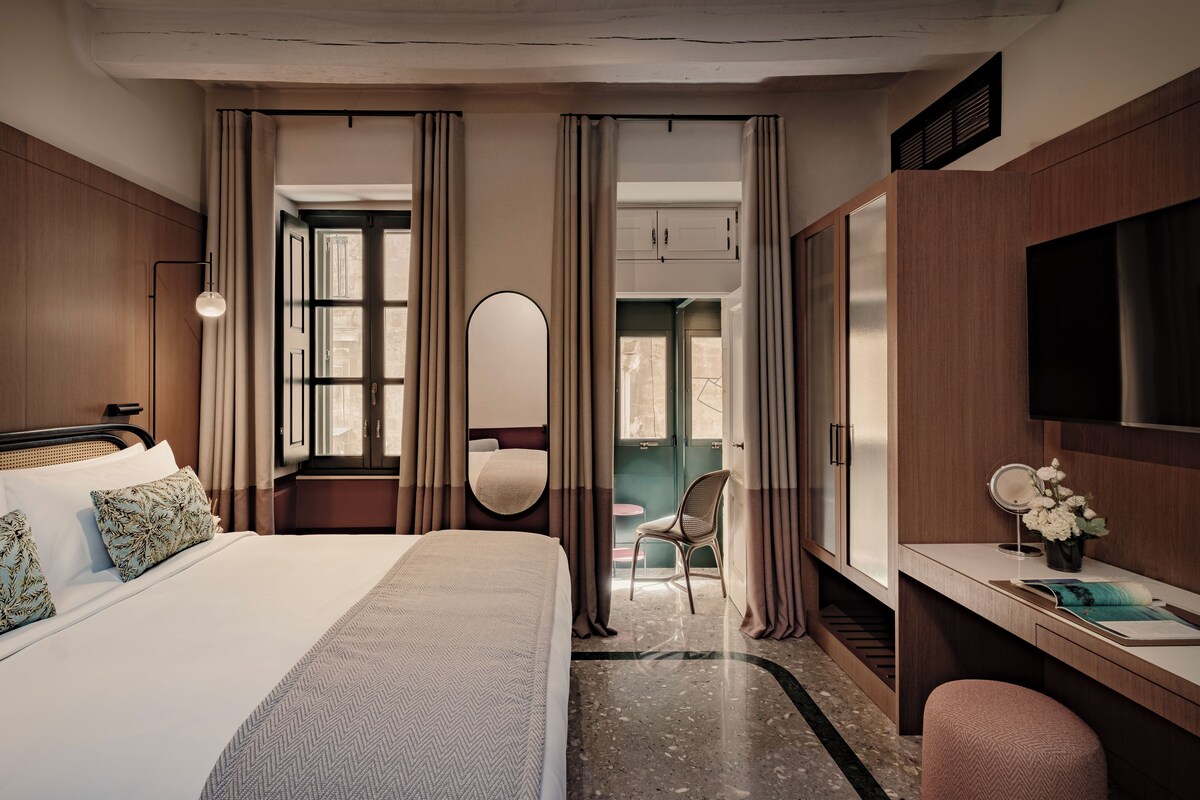 A hotel room with a bed, a desk, a chair, a TV, and a bathroom visible through a door.