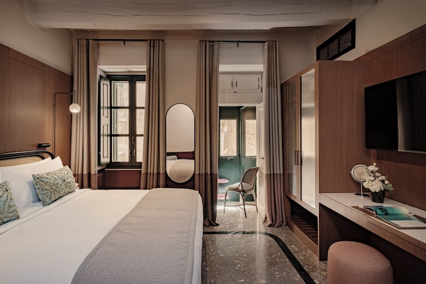 A hotel room with a bed, a desk, a chair, a TV, and a bathroom visible through a door.