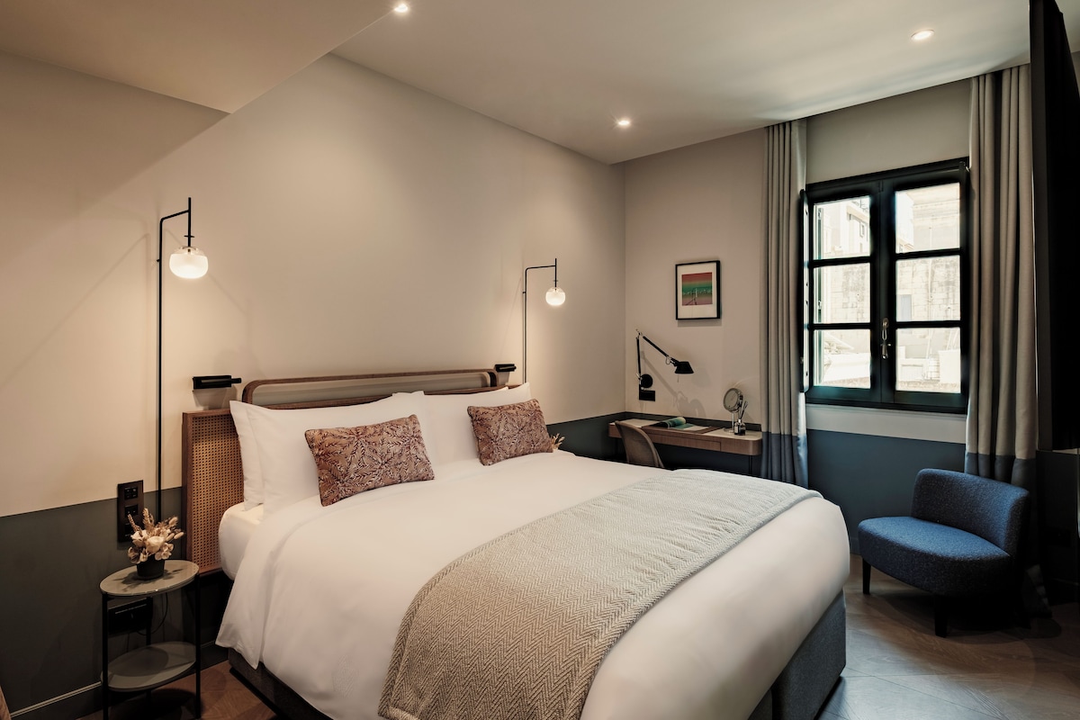 A hotel room with a large bed, bedside tables, a desk, and a chair.
