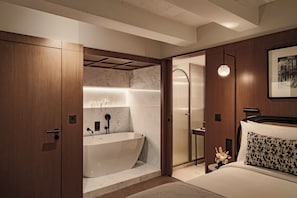 A modern bathroom with a freestanding bathtub, a shower area, and a bed with a patterned pillow. - Romègas Hotel (Valletta)