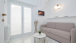 Una sala moderna con un sofá, una mesita con una planta, un radiador, una puerta y un estante de pared con el logo de Netflix.