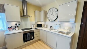 A modern kitchen with white cabinetry, a stainless steel range hood, a large wall clock, and a microwave.