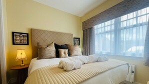 A hotel room with a large bed, a bedside table with a lamp, and a window with curtains.