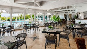 Un amplio espacio exterior con área de comedor, mesas y sillas, piscina y vistas a la vegetación circundante.