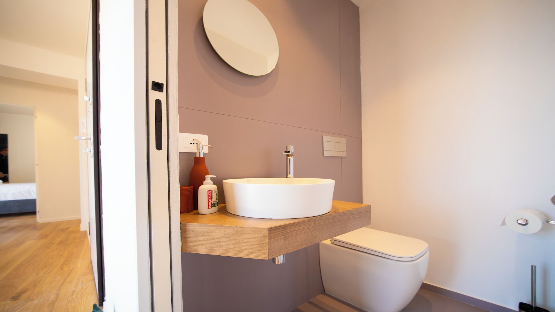 A modern bathroom with a round mirror, a white sink, and a toilet.