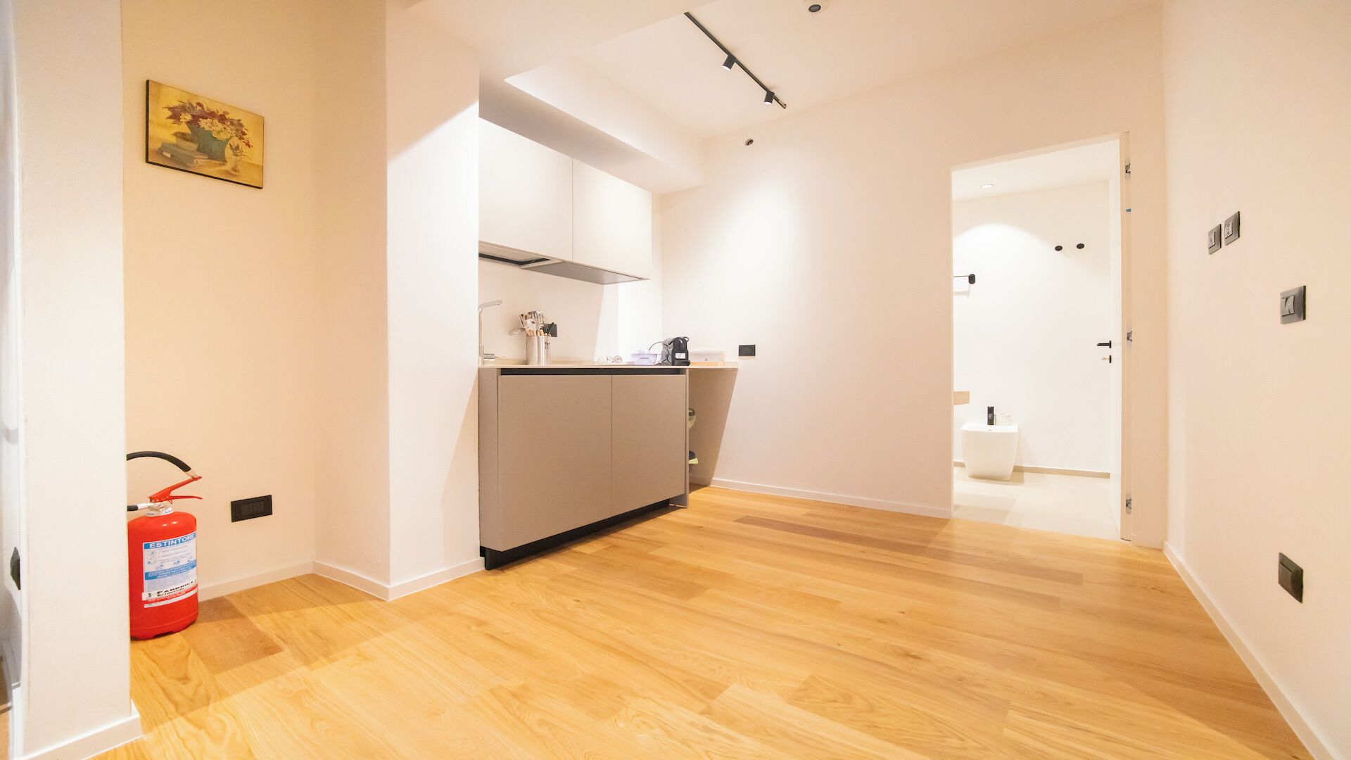 Een moderne keuken met een centraal eiland, houten vloeren en een brandblusser aan de linkerkant.