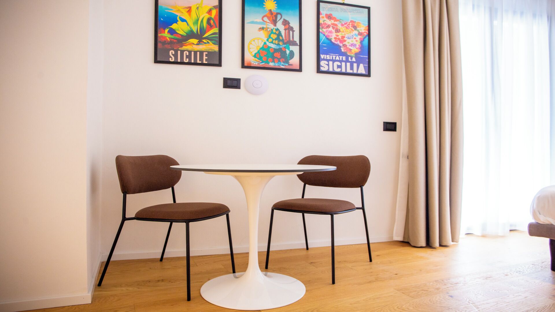 A dining area with a round table and two chairs, a wall-mounted light, and framed pictures.