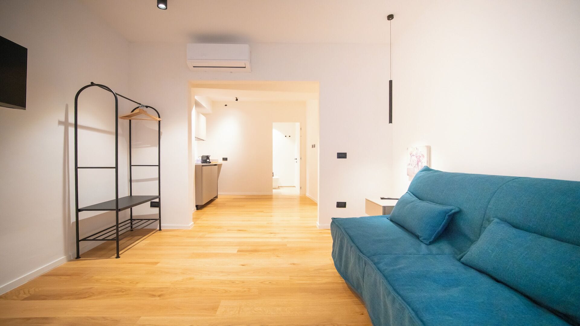 A modern living room with a blue sofa, a metal shelving unit, and a wooden floor.