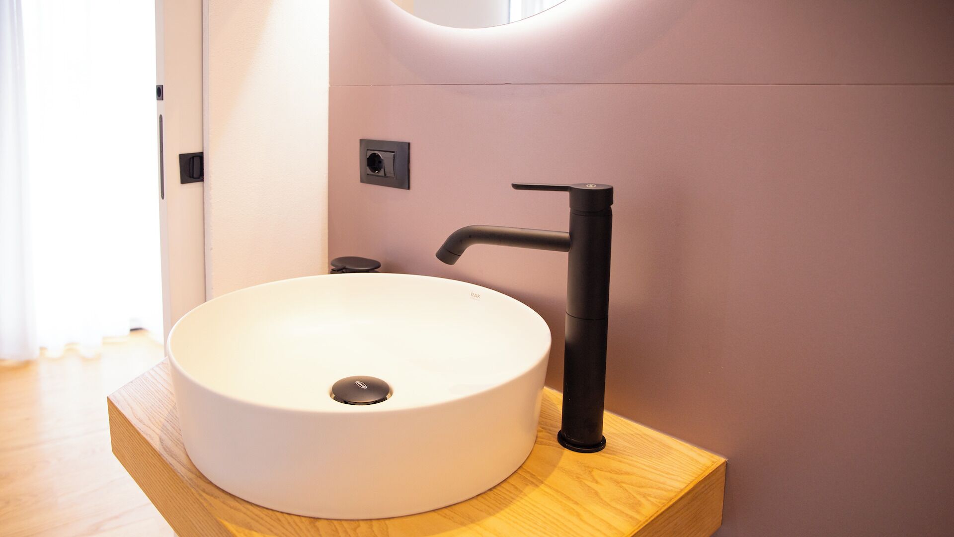 A modern bathroom with a round white sink, a black faucet, and a wooden countertop.