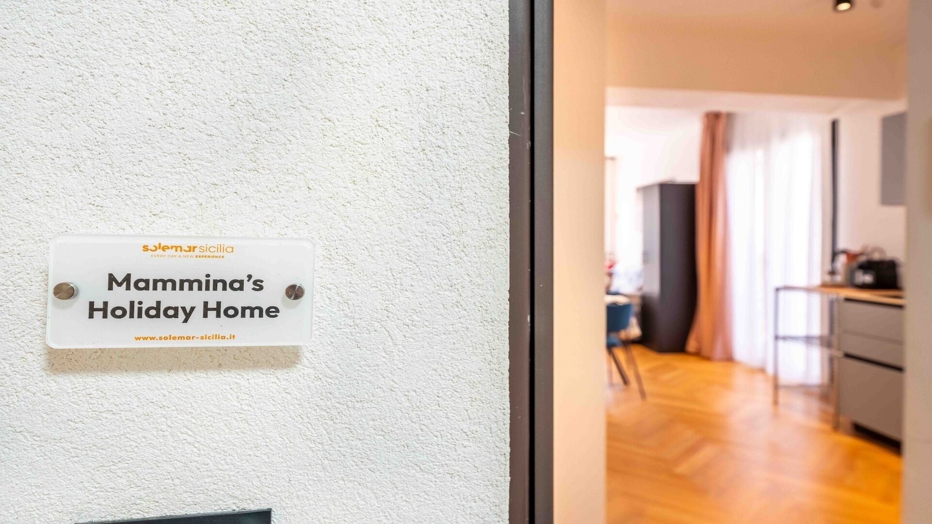 Une pancarte sur un mur indiquant « Mamma’s Holiday Home » et affichant l’adresse d’un site web.