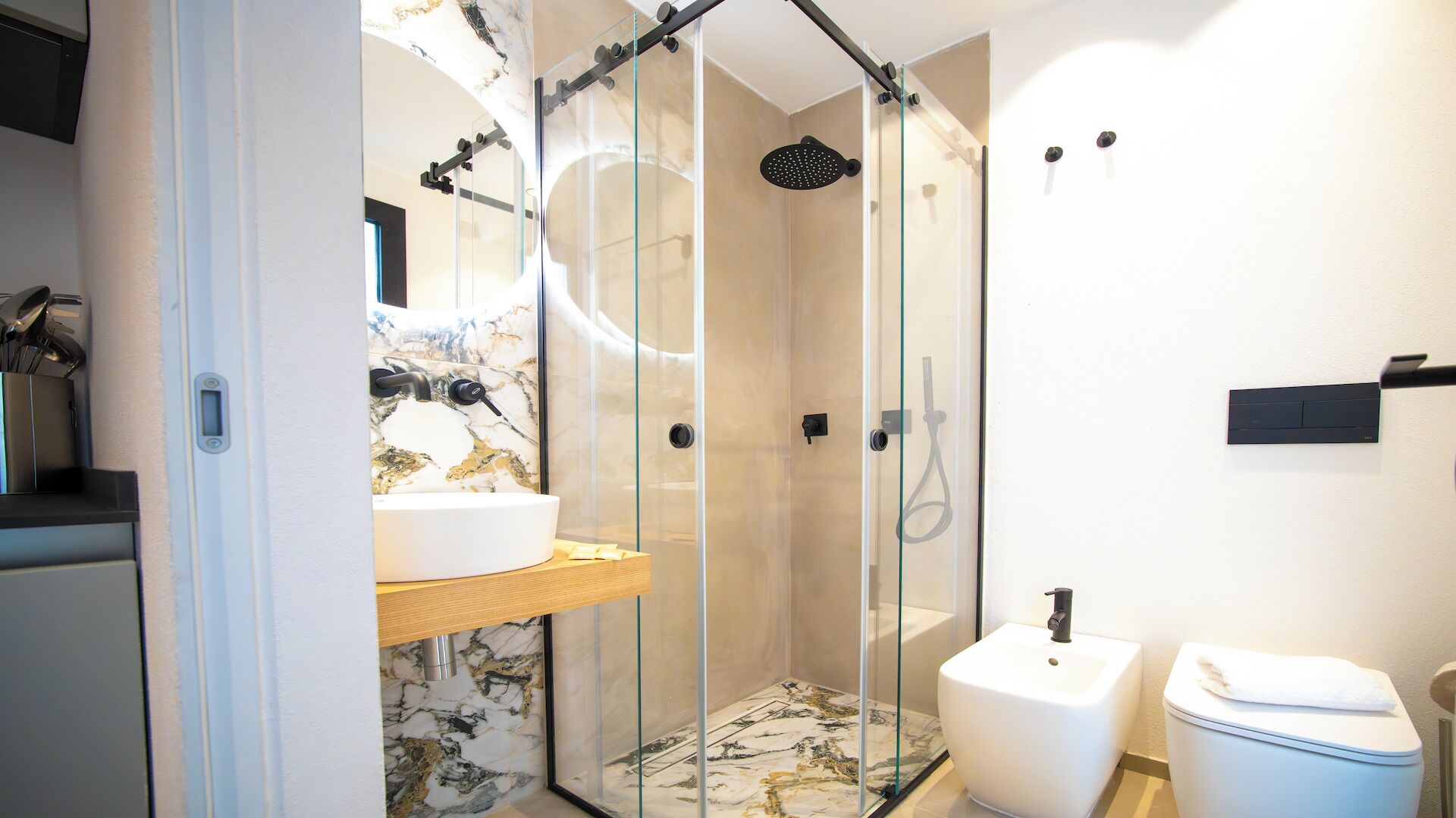 Une salle de bain moderne avec une douche à parois de verre, un meuble-lavabo recouvert de carreaux de marbre et des toilettes blanches.