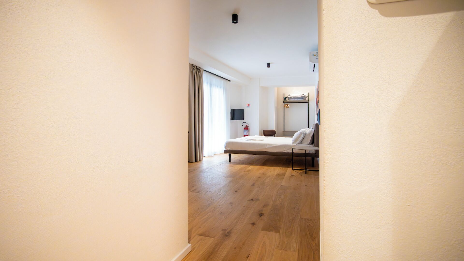 A hotel room with a bed, a chair, a small table, and a TV on the wall.