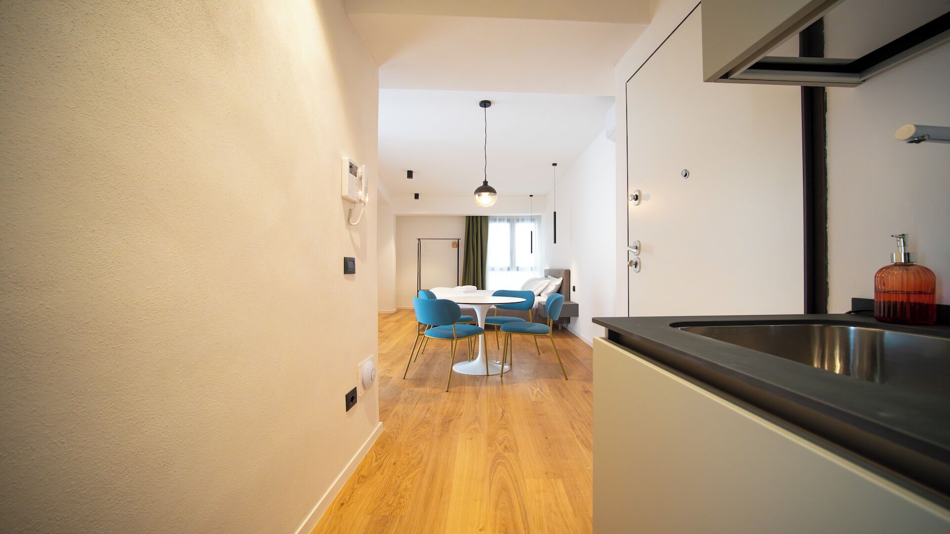 A modern kitchen with a stainless steel sink, a dining area with blue chairs, and a wooden floor.