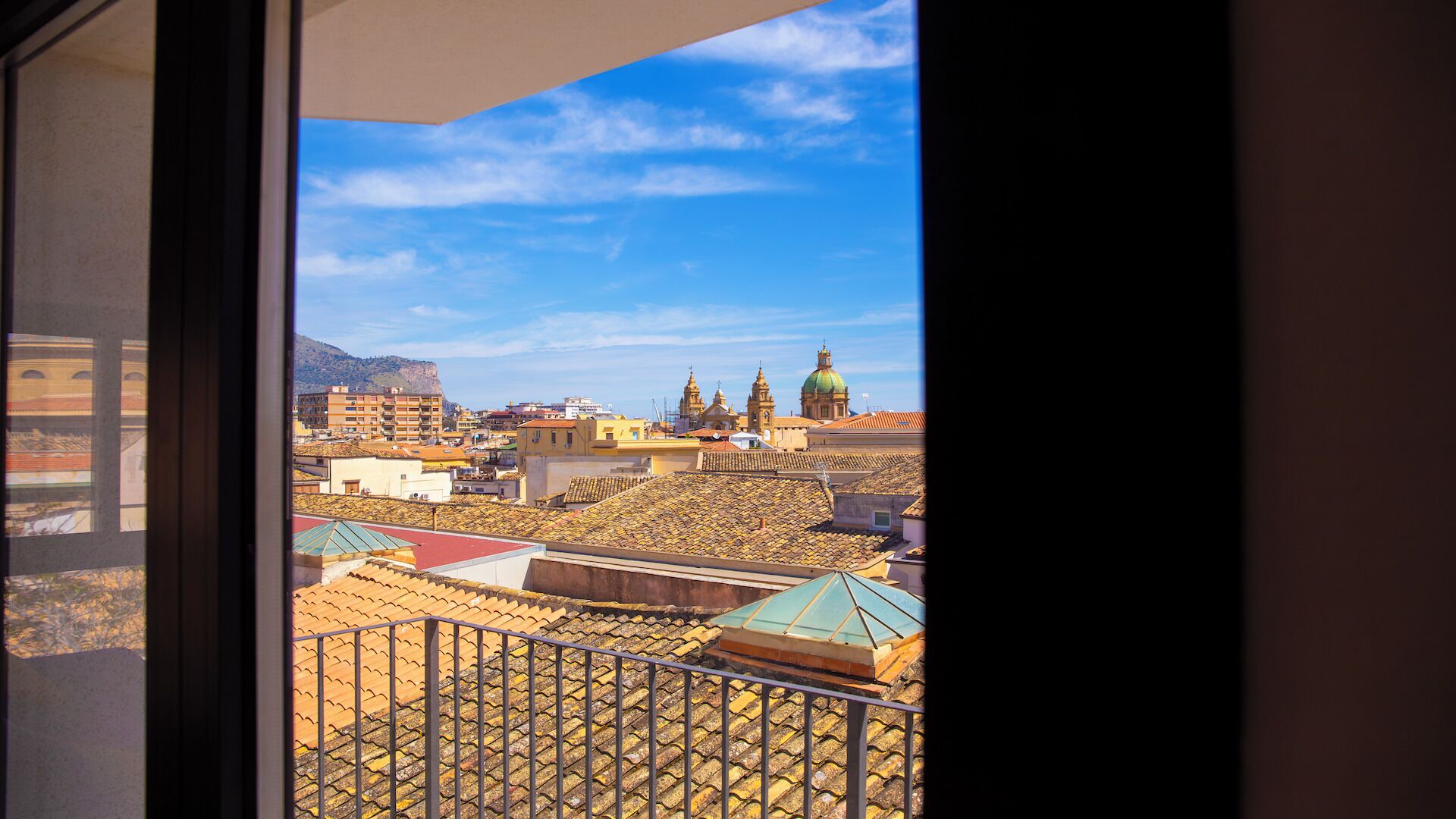 A view from a balcony with a metal railing, overlooking a cityscape with buildings and a green dome structure.