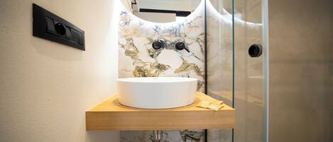 Une salle de bain avec un lavabo blanc posé sur une étagère en bois, un pare-baignoire en marbre et une douche à parois de verre.