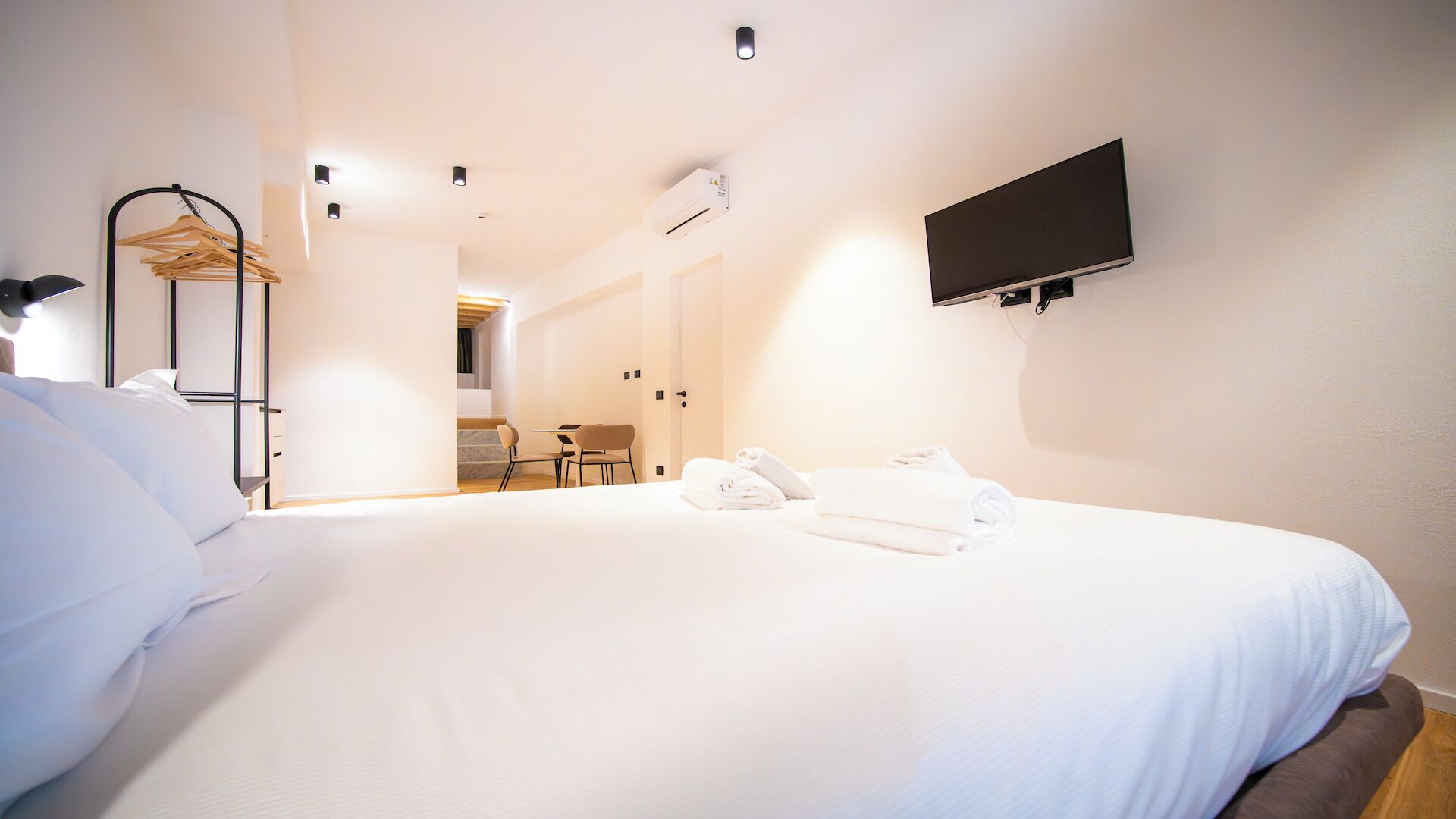 A hotel room with a large bed, a flat-screen TV mounted on the wall, a wooden chair, and a small table.