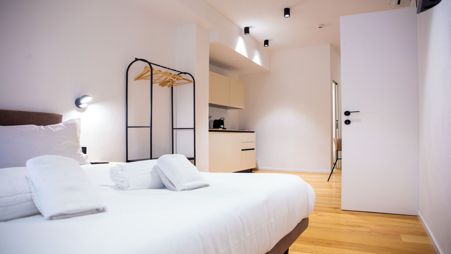 A modern hotel room with a bed, a wardrobe, a kitchenette, and a bathroom.