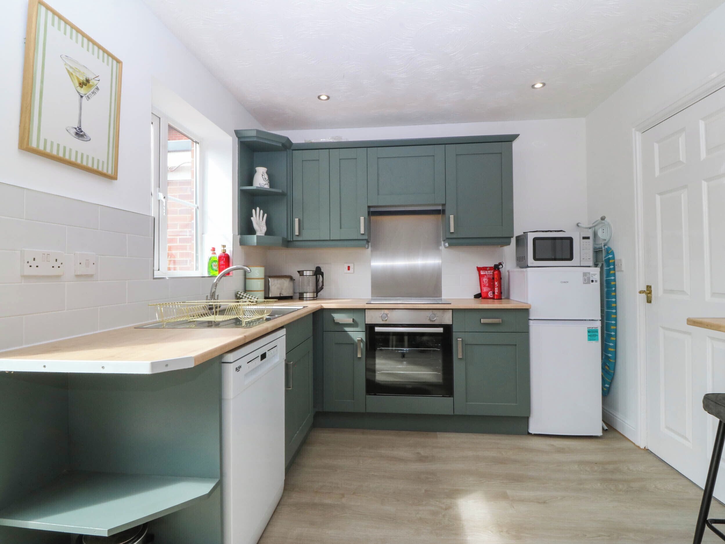 A kitchen with teal cabinets, a white dishwasher, a microwave, a toaster, and a stainless steel range hood.