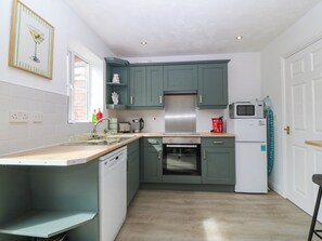 A kitchen with teal cabinets, a white dishwasher, a microwave, a toaster, and a stainless steel range hood. - Meadow View (Rhyl)