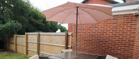 A patio with a table and chairs, a large umbrella, and a brick wall.