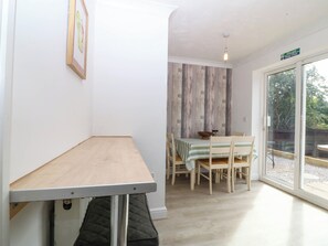 A dining area with a table and chairs, a wooden floor, a window with a view, and a fire exit sign. - Meadow View (Rhyl)