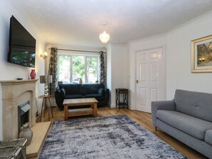 A living room with a fireplace, a sofa, a coffee table, and a television mounted on the wall. - Meadow View (Rhyl)