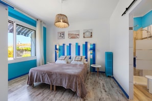A bedroom with a bed, a window, a wall-mounted shelf, and a radiator.