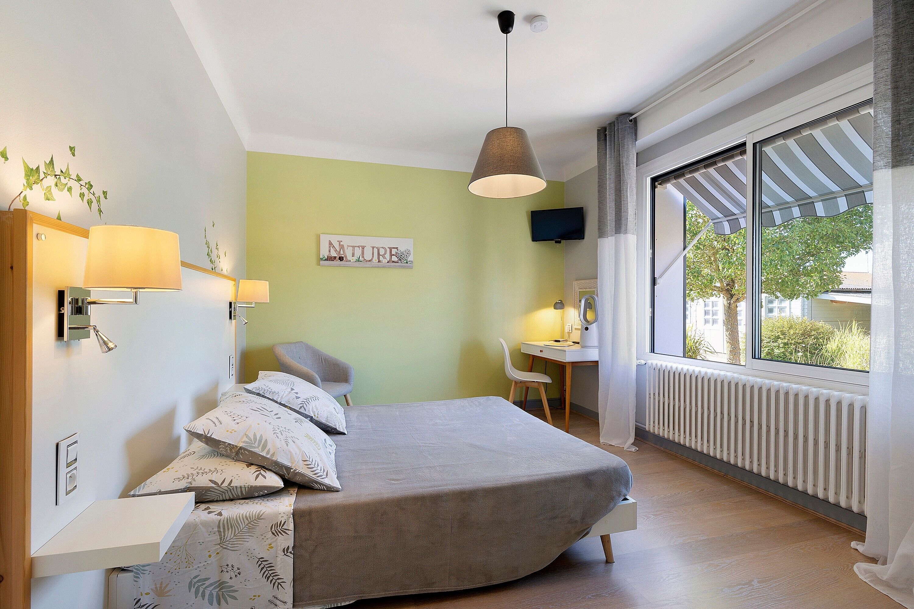 A bedroom with a bed, bedside lamps, a desk, a chair, a television, and a window with a view.