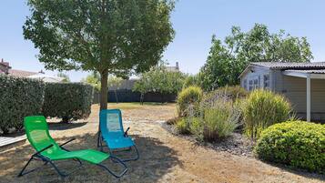 Een tuin met twee groene stoelen, een boom en een gebouw op de achtergrond.