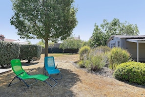 A garden with two green chairs, a tree, and a building in the background.